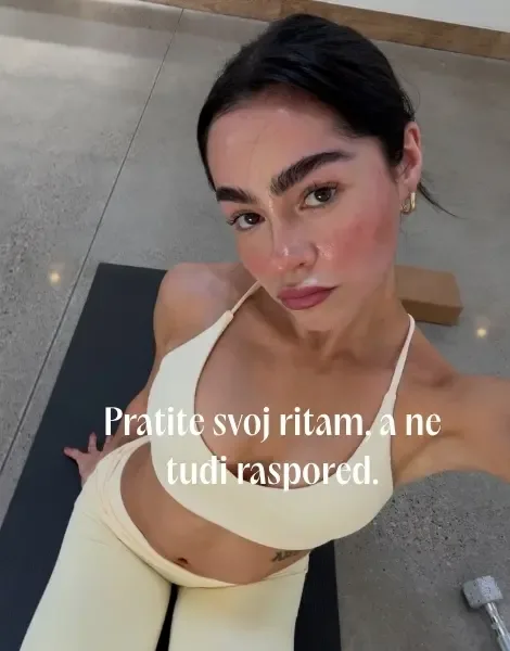 Devojka u svetložutom sportskom kompletu pravi selfi odozgo sedeći na joga prostirci