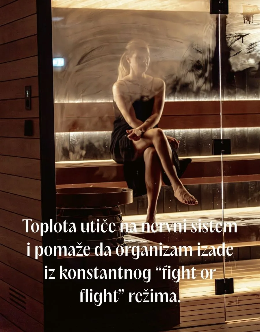 Plavokosa žena u crnoj haljini, prekrštenih nogu, sedi i uživa